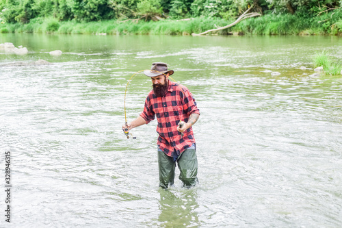 Fisher masculine hobby. Fishing requires to be mindful and fully present in moment. Fisher fishing equipment. Rest and recreation. Fish on hook. Brutal man stand in river water. Man bearded fisher