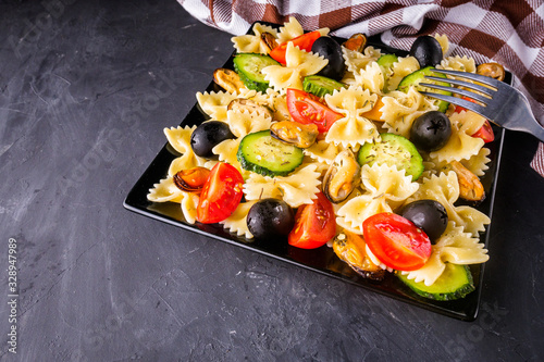 tasty pasta salad with tomato cucumber and olives on a dark stone background