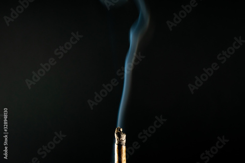 A Lit Brown Cannabis Cigar With a line of Thick Smoke Coming From it on a Black Background