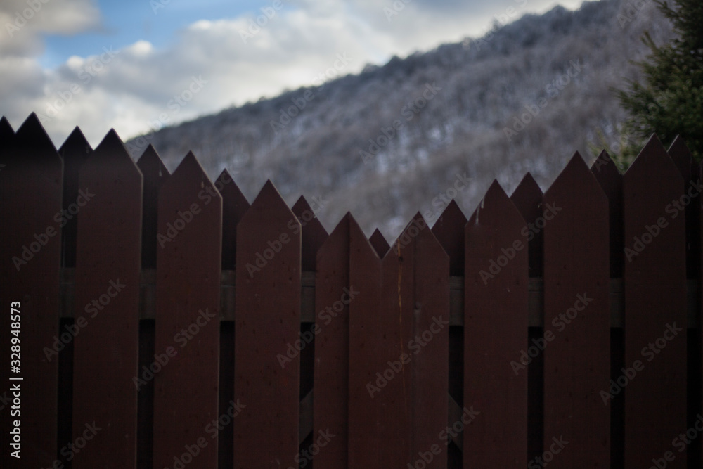 Wooden fence at the house in the mountains. Toothed fence on the background of a hillside. The fence around the building made of wood. Wooden fence at the house in the mountains. Toothed fence on the background of a hillside. The fence around the building made of wood.