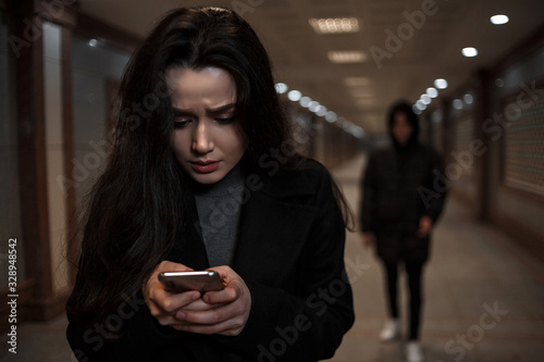 a young beautiful woman walks through an underground passage at night, followed by a man in dark clothing with a hood on his head. a woman tries to dial the number of the rescue service on the phone
