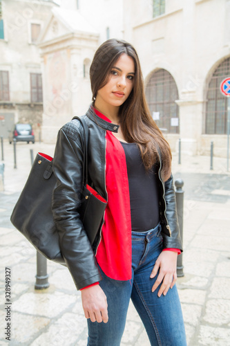 Donna italiana molto bella con abbigliamento diurno con canotta nera e camicia rossa una giacca di pelle nera e borsa nel Centro Storico di Bisceglie tra Trani Molfetta e Andria