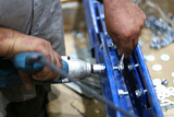 One warehouse worker in with power tool tightening screw during rack arrangement erection work