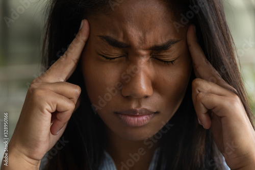 Unhealthy African American girl touch massage temples suffer from headache or migraine at workplace, tired biracial woman employee struggle with dizziness or blurry vision, overwork, fatigue concept photo
