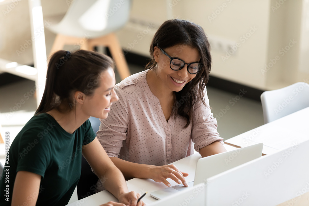 Multiracial smiling female colleagues busy cooperating working on laptop discuss business project in office together, multiethnic diverse businesswomen talk collaborate using computer at workplace Multiracial smiling female colleagues busy cooperating working on laptop discuss business project in office together, multiethnic diverse businesswomen talk collaborate using computer at workplace