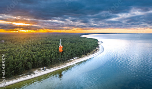 Fototapeta Naklejka Na Ścianę i Meble -  Sunset over coastline at Baltic sea. Aerial view on lighthouse and forest in background. 
