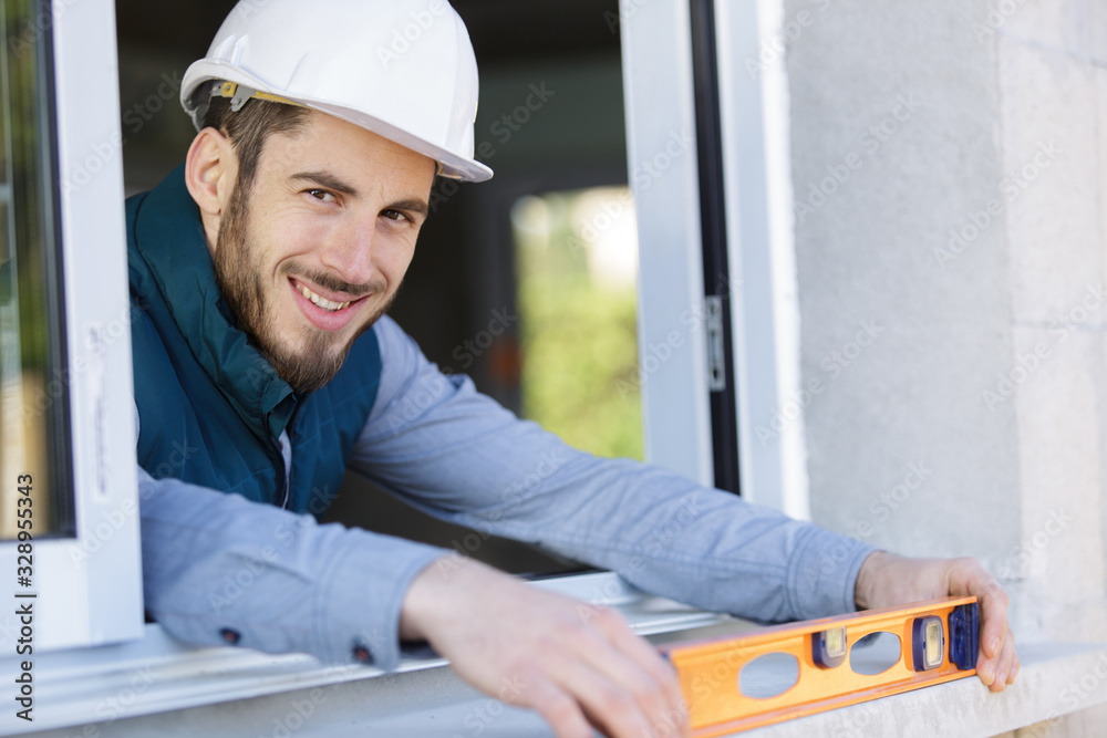 happy male builder in protective helmet using a level happy male builder in protective helmet using a level