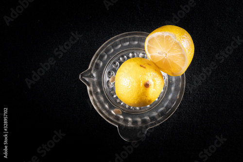 Lemon cut in half, on a glass lemon squeezer. Black background