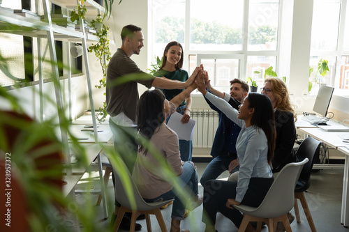 Excited multiracial colleagues give high five celebrate shared business success victory at briefing, overjoyed diverse businesspeople engaged in teambuilding activity at office meeting together photo