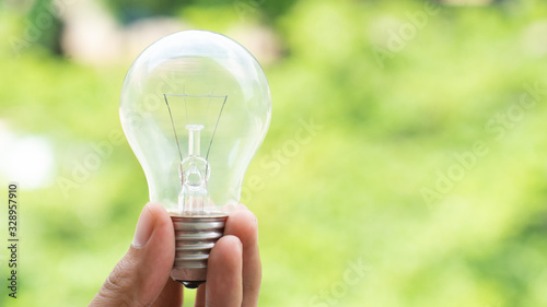 Hand holds light bulb with green trees background