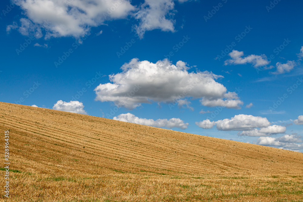 Fluffy clouds and a blue sky over a field following harvesting