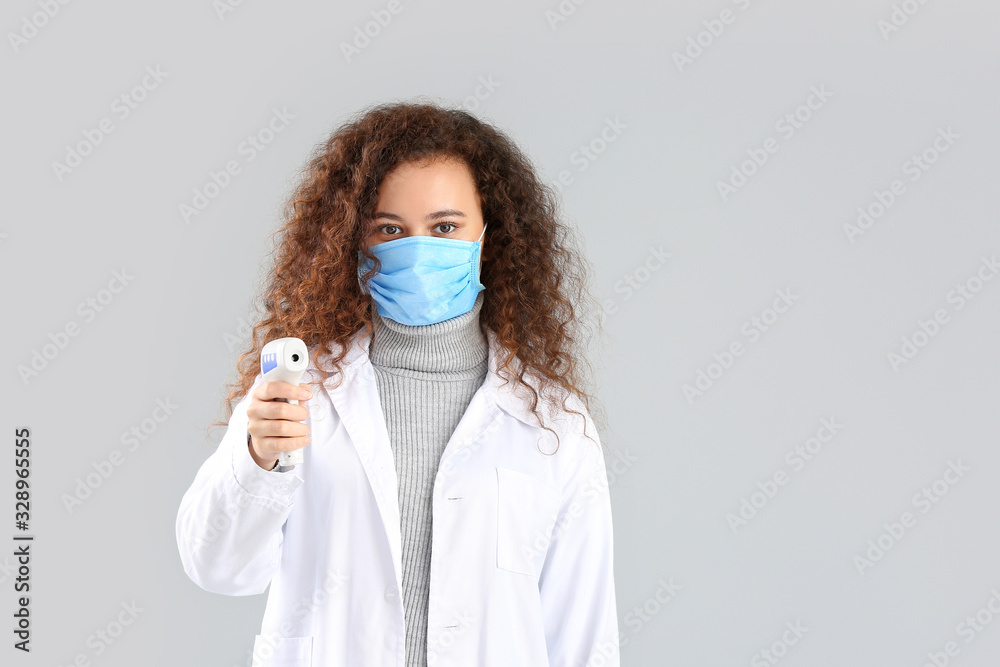 Female doctor with protective mask and thermometer on grey background. Concept of epidemic Female doctor with protective mask and thermometer on grey background. Concept of epidemic