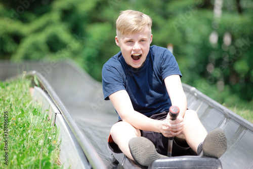 Fototapet Happy teen boy riding at bobsled roller coaster rail track in summer amusement p