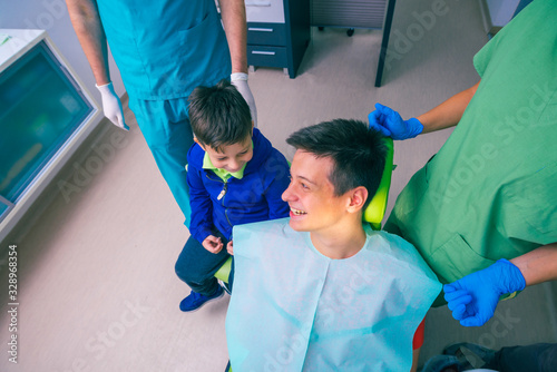Fényképezés Teenage boy with his younger brother sitting on the dentist chair waiting for a