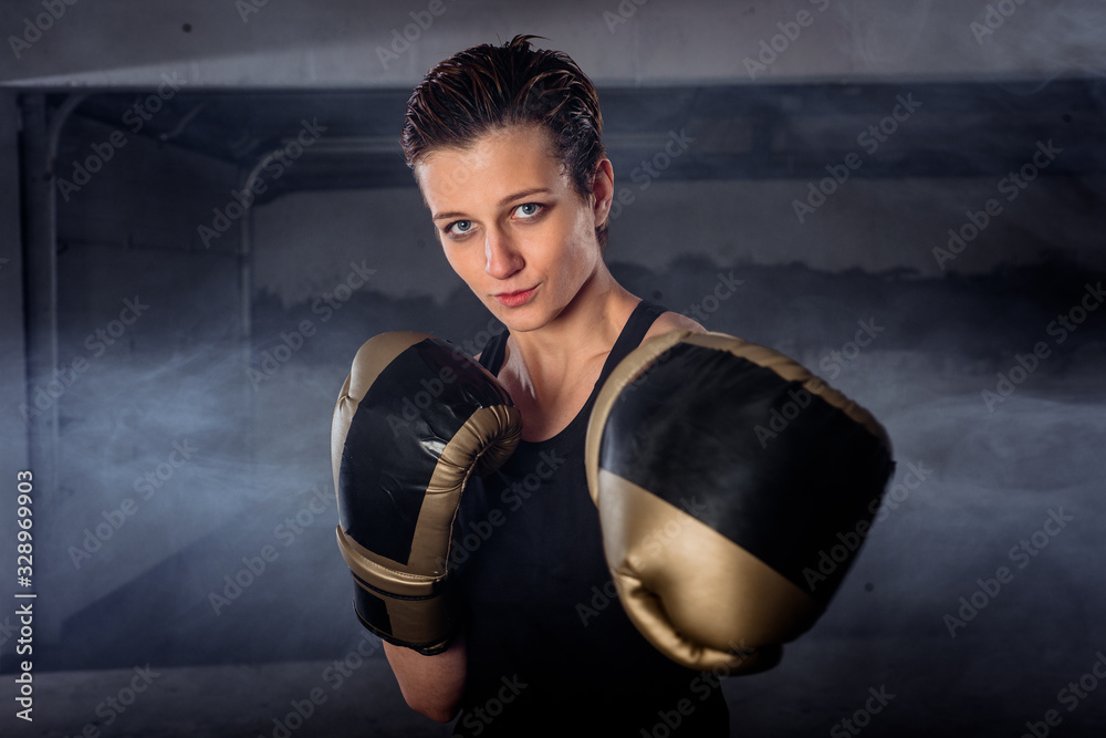 Closeup image with smokey background of a female boxer punching with boxing gloves and looking at the camera