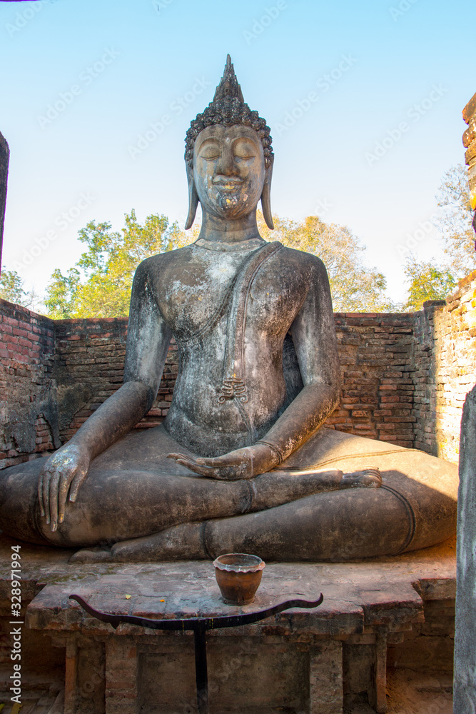 Obraz premium An old buddha statue in a historical park with tree and blue sky as background