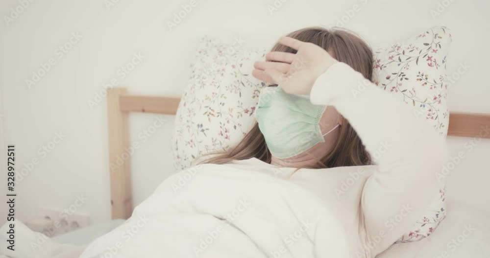 Woman with face mask measures temperature in bed quarantine protection virus coronavirus medical thermometer Woman with face mask measures temperature in bed quarantine protection virus coronavirus medical thermometer