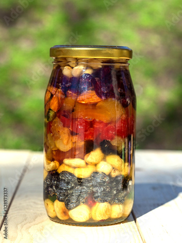 Healthy mix of dry fruits and nuts in honey in glass jar on a wooden table