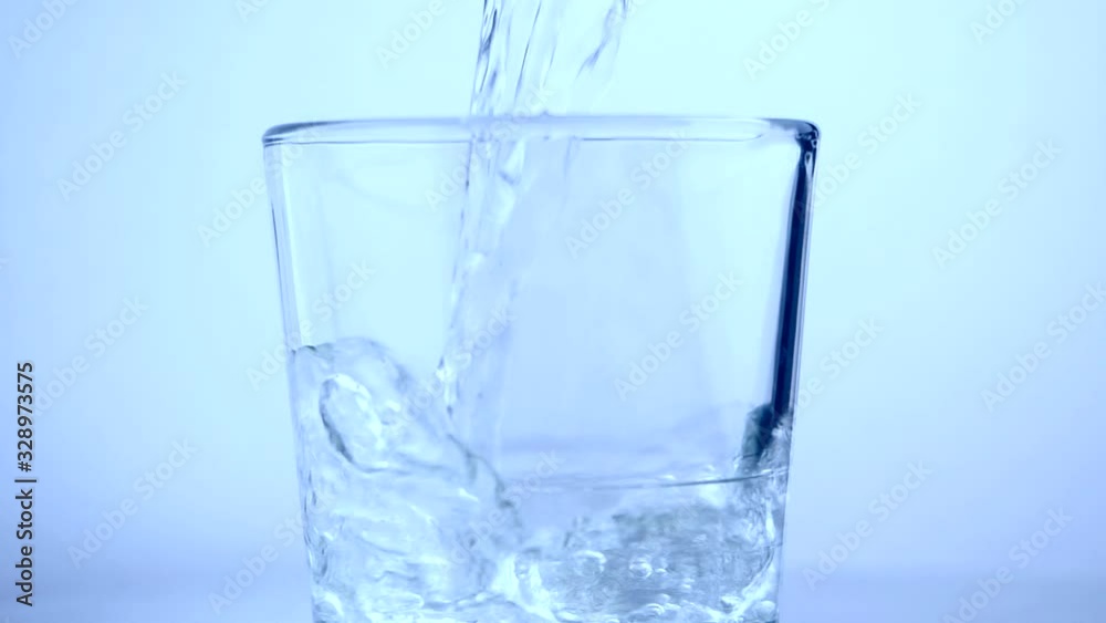 Close-up of water pouring into transparent glass in slow motion on white background