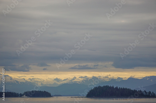 Alaska, USA: Snow-capped mountains under a cloudy sky, a cruise ship sailing through islands in the Inside Passage.