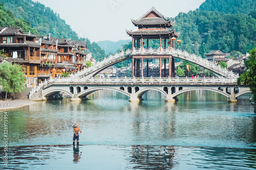 Man fishing on water at the river Tuojiang in the Ancient city of China, Fenghuang. Traditional Chinese bridge. Village of the phoenix. Romantic China photo