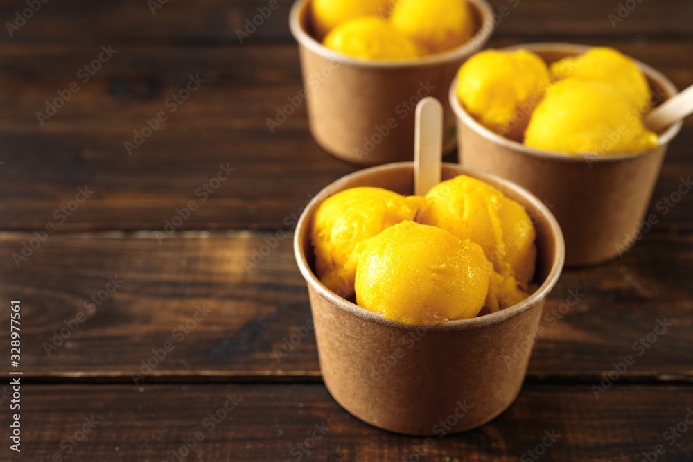 Delicious mango ice sorbet in paper cups on wooden background in rustic style