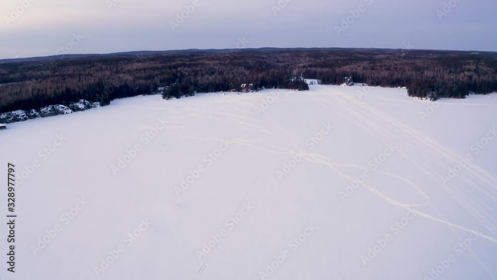 Drone shot flying towards a large cabin in the woods along a frozen lake in winter. Drone shot flying towards a large cabin in the woods along a frozen lake in winter.