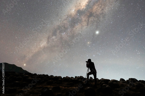 silhouette of photographer with camera next to the Milky Way galaxy on the hill.