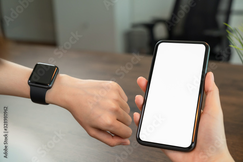 Close-up of hand holding smartphone and looking smartwatch.