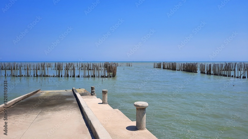 Concrete pier beside seashore with bamboo pole for protection wave and blue sky background.