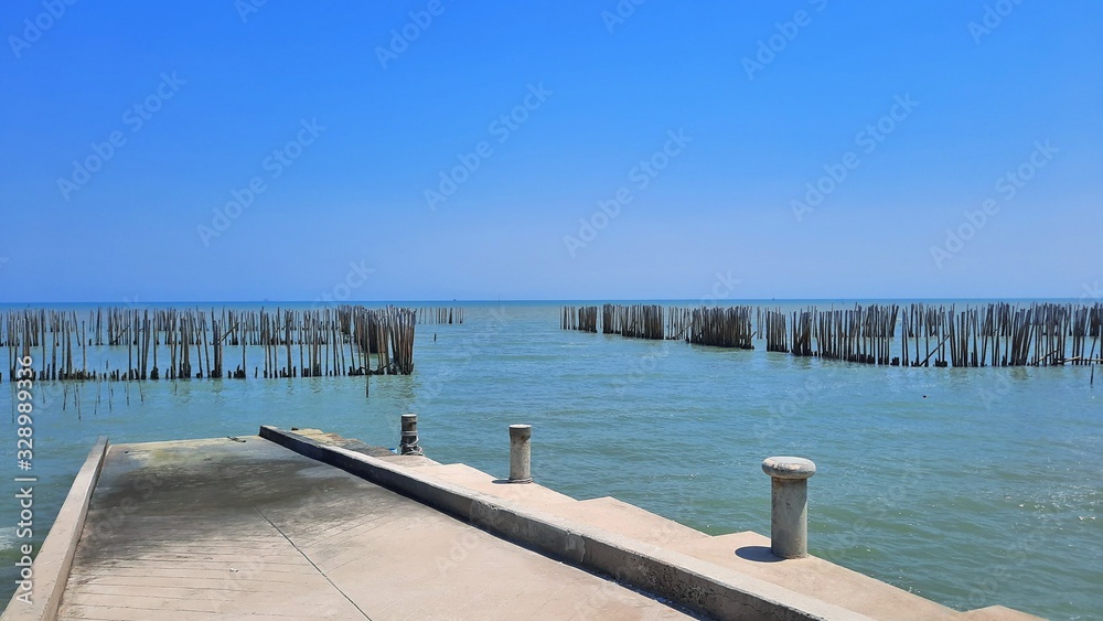 Concrete pier beside seashore with bamboo pole for protection wave and blue sky background.