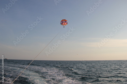 A young man and a girl are flying on a double parachute behind a boat over the sea.