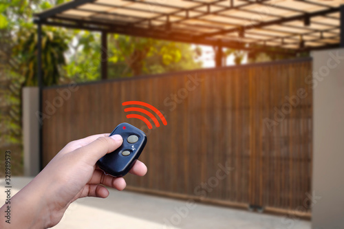 Closeup hand holding and using remote control to open or close the automatic wooden gate with home blurred background. Home remote control concept. concept. photo