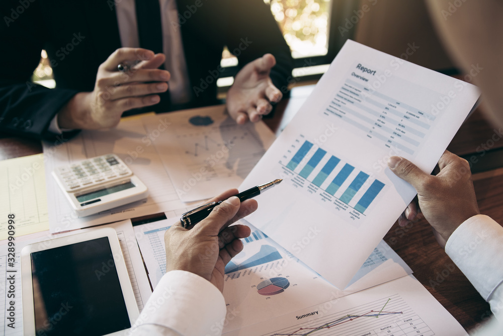 © wutzkoh - Manager calculates about the company finances by pressing on the calculator on the table with the employee explaining the summary report of the company cost at the office. © wutzkoh - Manager calculates about the company finances by pressing on the calculator on the table with the employee explaining the summary report of the company cost at the office.