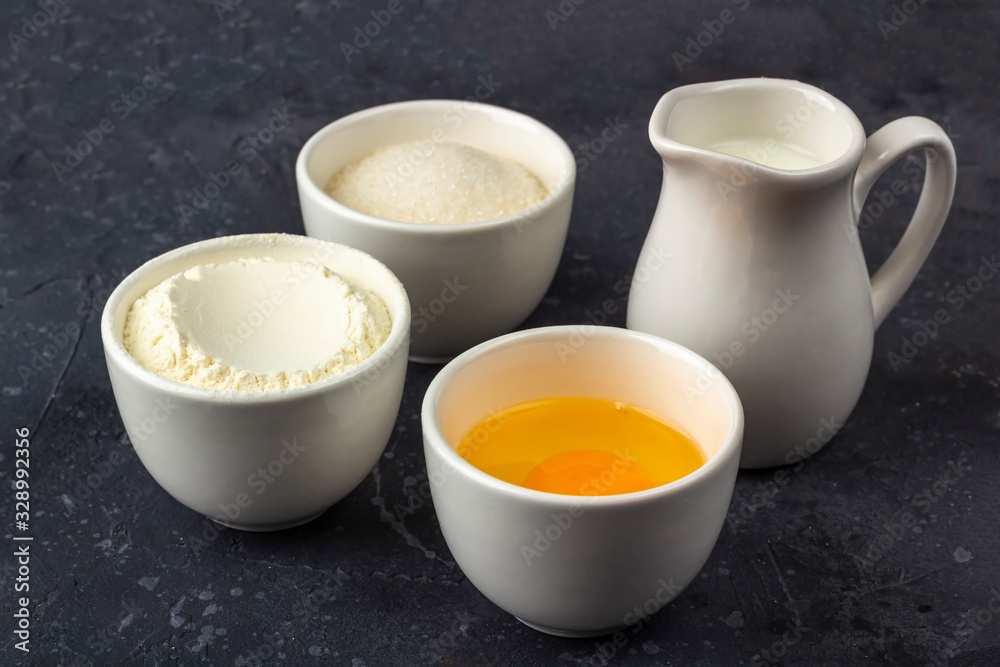 Baking background. Ingredients for cooking cake (flour, egg, sugar, milk) in bowls on dark table. Food concept. Close up/ Baking background. Ingredients for cooking cake (flour, egg, sugar, milk) in bowls on dark table. Food concept. Close up/