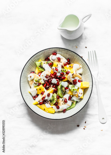Greek yogurt and tropical fruit salad for breakfast, snack, dessert. Salad with greek yogurt, banana, mango, kiwi, pomegranate seeds and flaxseeds on a gray background, top view