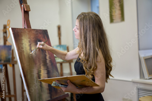 Fotografi Woman artist in art studio paints a picture, profile portrait