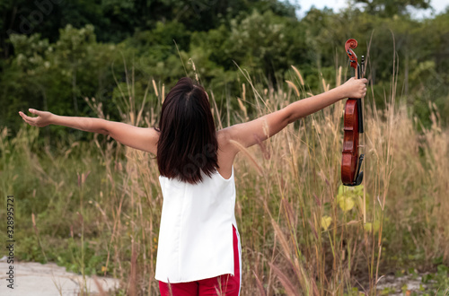 Back side of woman holding violing in hand and raise up in the air,model posing in a park,blurry lightaround photo