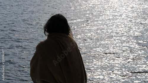 Slihouette of Back of Female Cloaked With Towel on Bow of Boat With Sunlight Sea Reflection, Slow Motion photo