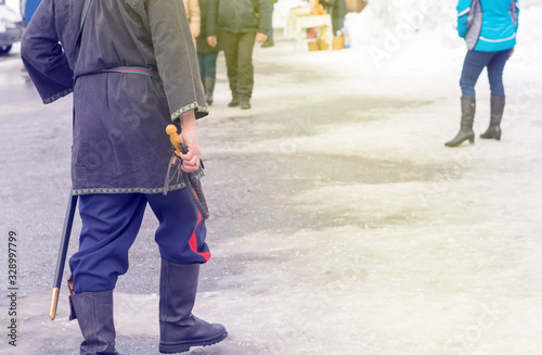 Cossack whip in the hand of a Cossack who goes in national costume, in kirzov boots and with a saber in winter on a crowded street photo