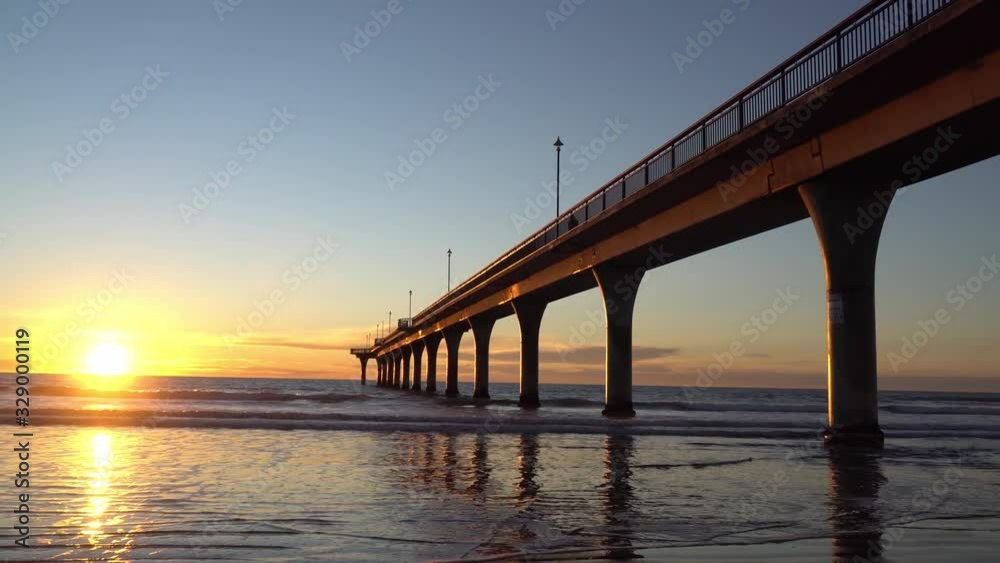 Tracking shot of sunrise above the sea in New Brighton, Christchurch of New Zealand; Waves under the bridge beating on the beach Tracking shot of sunrise above the sea in New Brighton, Christchurch of New Zealand; Waves under the bridge beating on the beach
