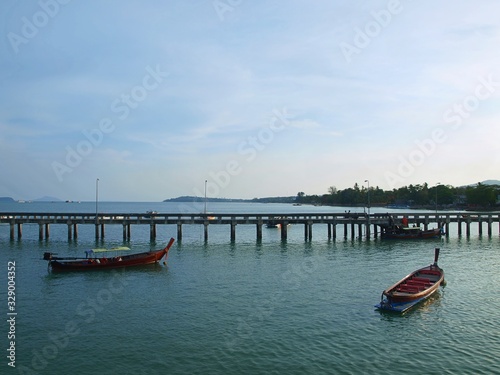 Anchored boats at the sea near long bridge.  Two traditional Thai longtailboats near pair. Panoramic view from the water.  photo