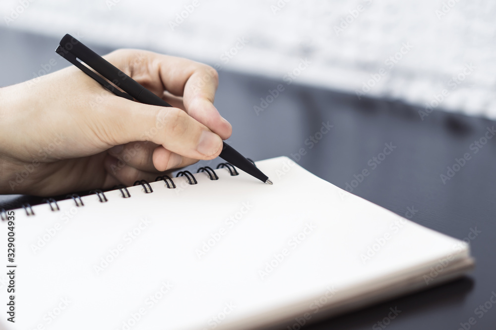 Man writes with a pen in diary in a sunny office, business and education concept. Close up Man writes with a pen in diary in a sunny office, business and education concept. Close up