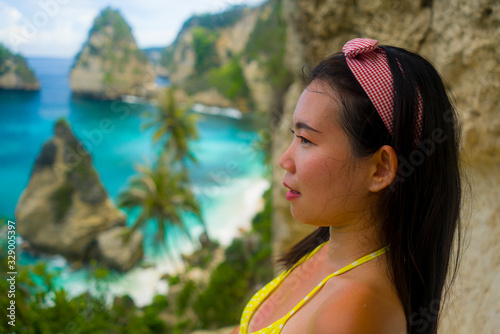 Summer holidays portrait of young beautiful and happy Asian Chinese woman in bikini enjoying amazing sea scene at tropical paradise beach with diamond shape rock cliff