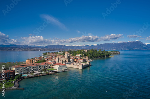 Fototapeta Naklejka Na Ścianę i Meble -  Sirmione town, Lake Garda, Italy. Aerial view of Sirmione. The historical part of the city.  In the background mountains in the snow and blue sky.  Side view of the island.