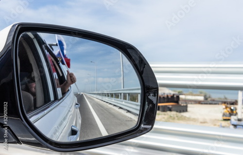 Car mirror with reflection of the road and the Russian flag