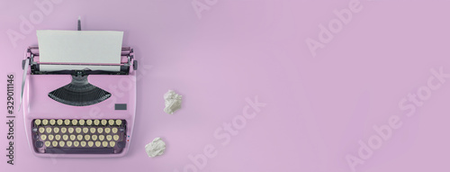 A pink vintage typewriter with pink background and two paper balls. 