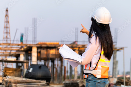 Asian woman civil engineer paper plan building architect wearing white safety helmet look at contruction site..