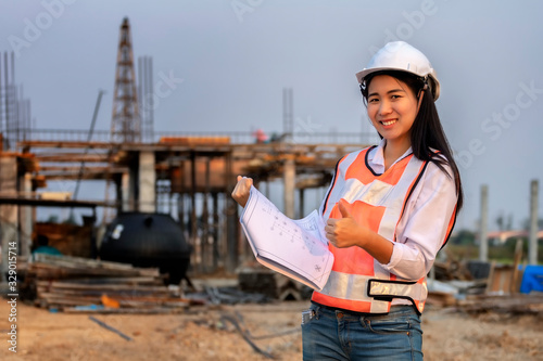 Asian woman civil engineer paper plan building architect wearing white safety helmet look at contruction site..