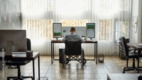 Wallpaper Mural Feeling upset. Back view of tired young male trader in a wheelchair bowed his head while working at workplace with three computer monitors in the modern office. Disability concept Torontodigital.ca